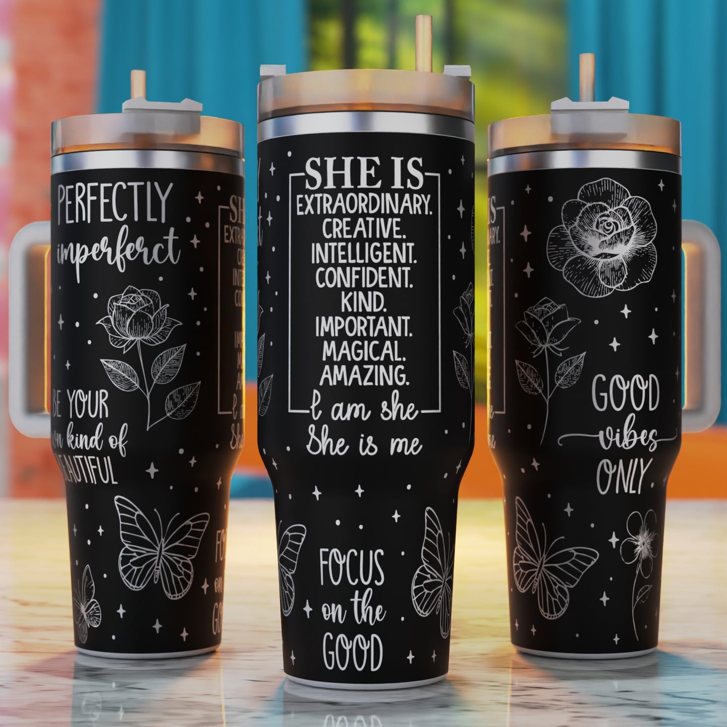 Three black tumblers with motivational quotes and designs on a wooden surface.