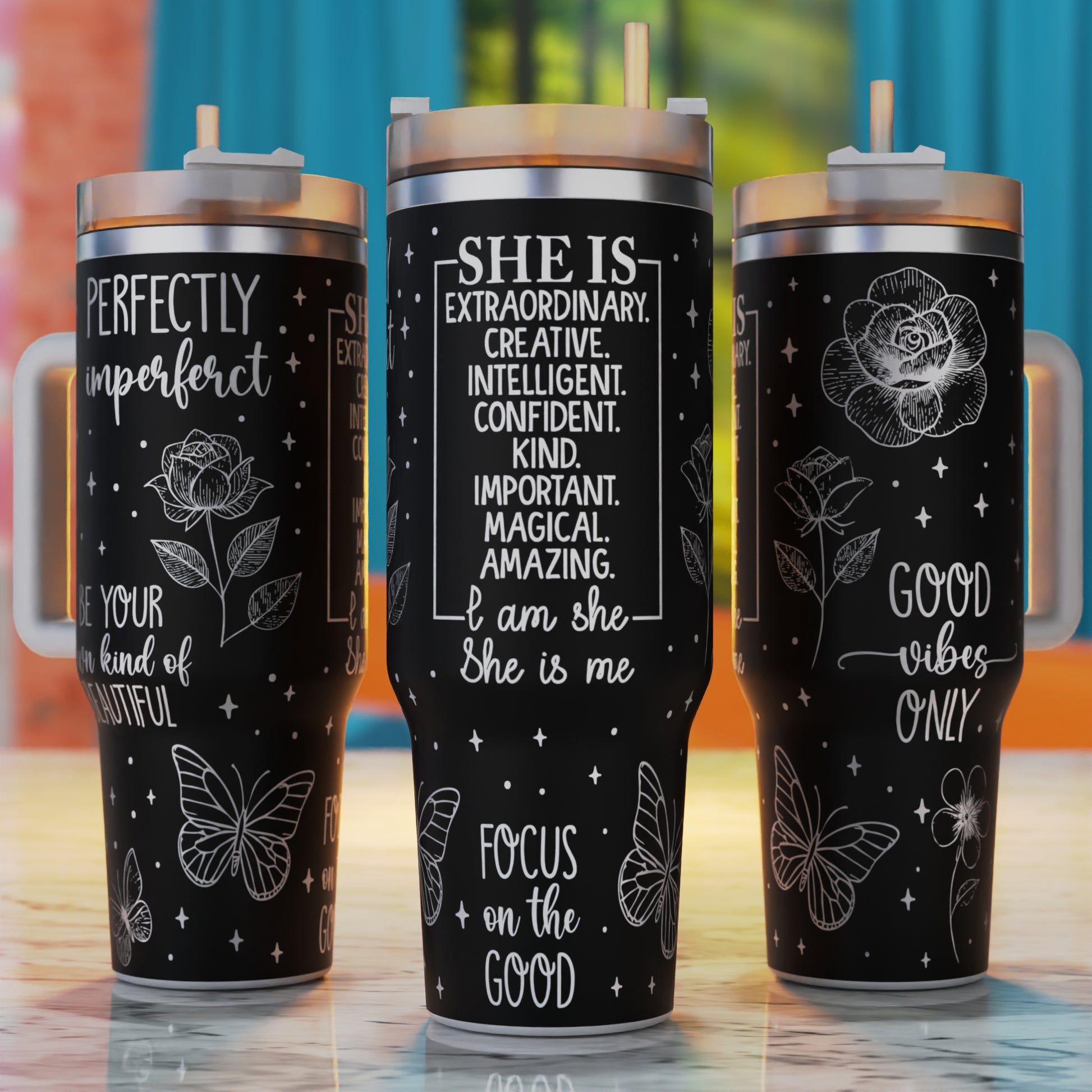 Three black tumblers with motivational quotes and designs on a wooden surface.